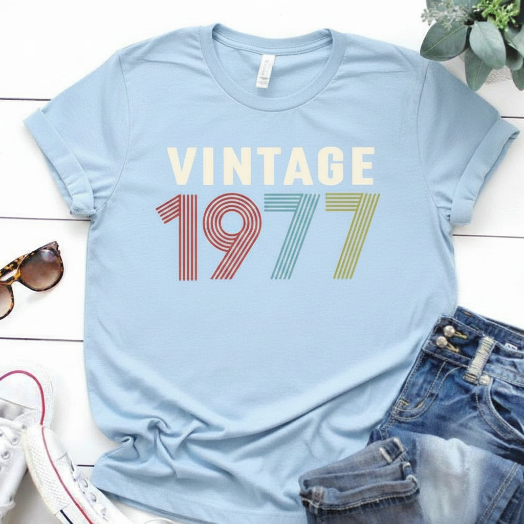 Light blue t-shirt with 'Vintage 1977' text on a white surface with sunglasses and jeans.