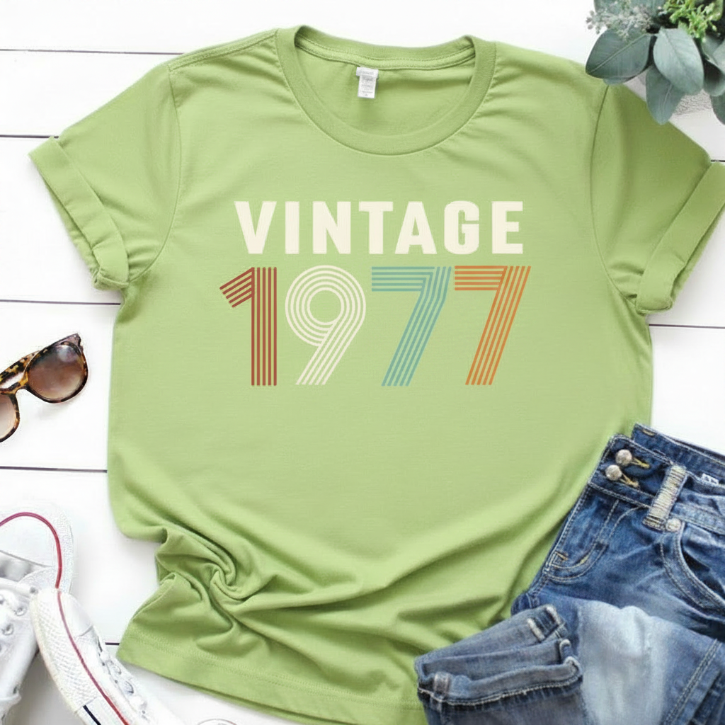 Black t-shirt with 'Vintage 1977' design on a white surface with jeans and sunglasses.