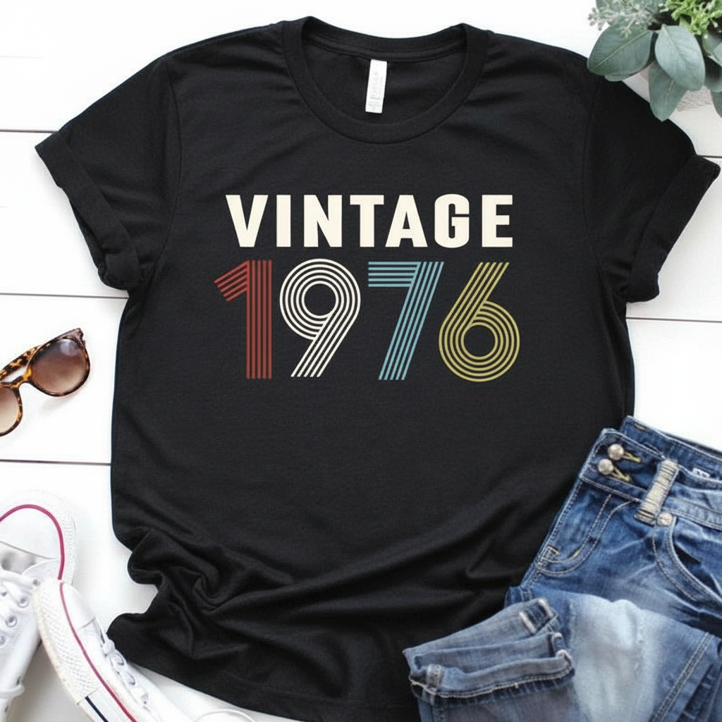 Black t-shirt with 'Vintage 1976' design on a white surface with sunglasses and jeans.