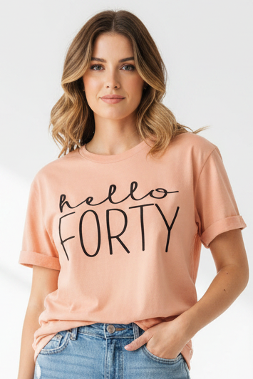 A woman wearing a peach-colored t-shirt with 'hello FORTY' printed in black script and block lettering, paired with blue jeans against a light gray background.