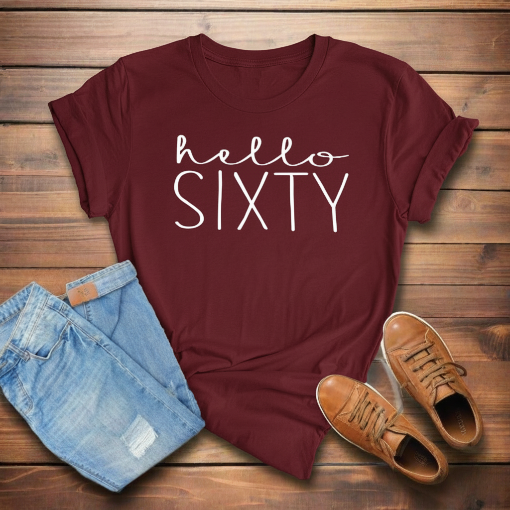 Maroon t-shirt with 'hello SIXTY' text, paired with blue jeans and brown shoes on a wooden surface.