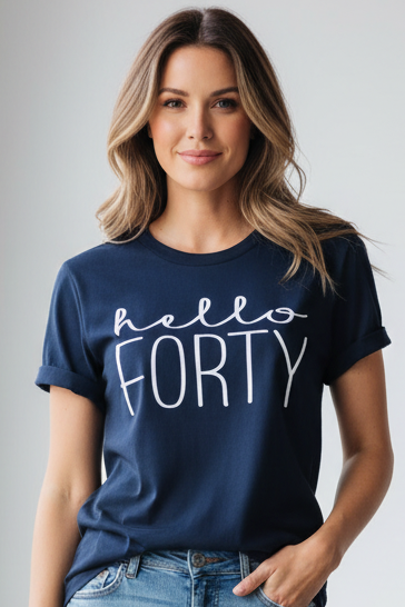 A woman wearing a navy blue t-shirt with 'hello FORTY' printed in white script across the chest, paired with blue jeans, set against a plain light gray studio background.