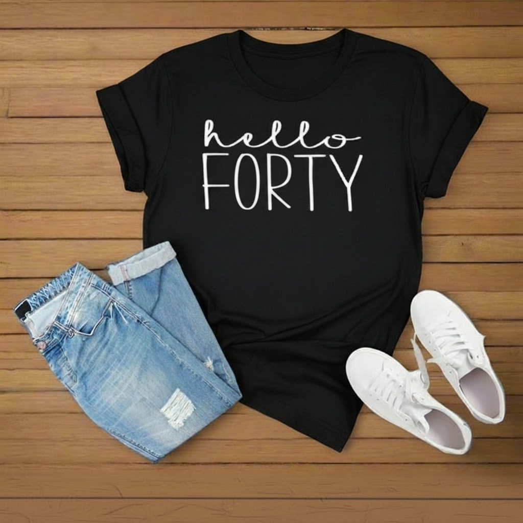 A black short-sleeve T-shirt with white text reading 'hello FORTY' is styled in a flat lay on a wooden surface with light blue denim shorts and white sneakers.