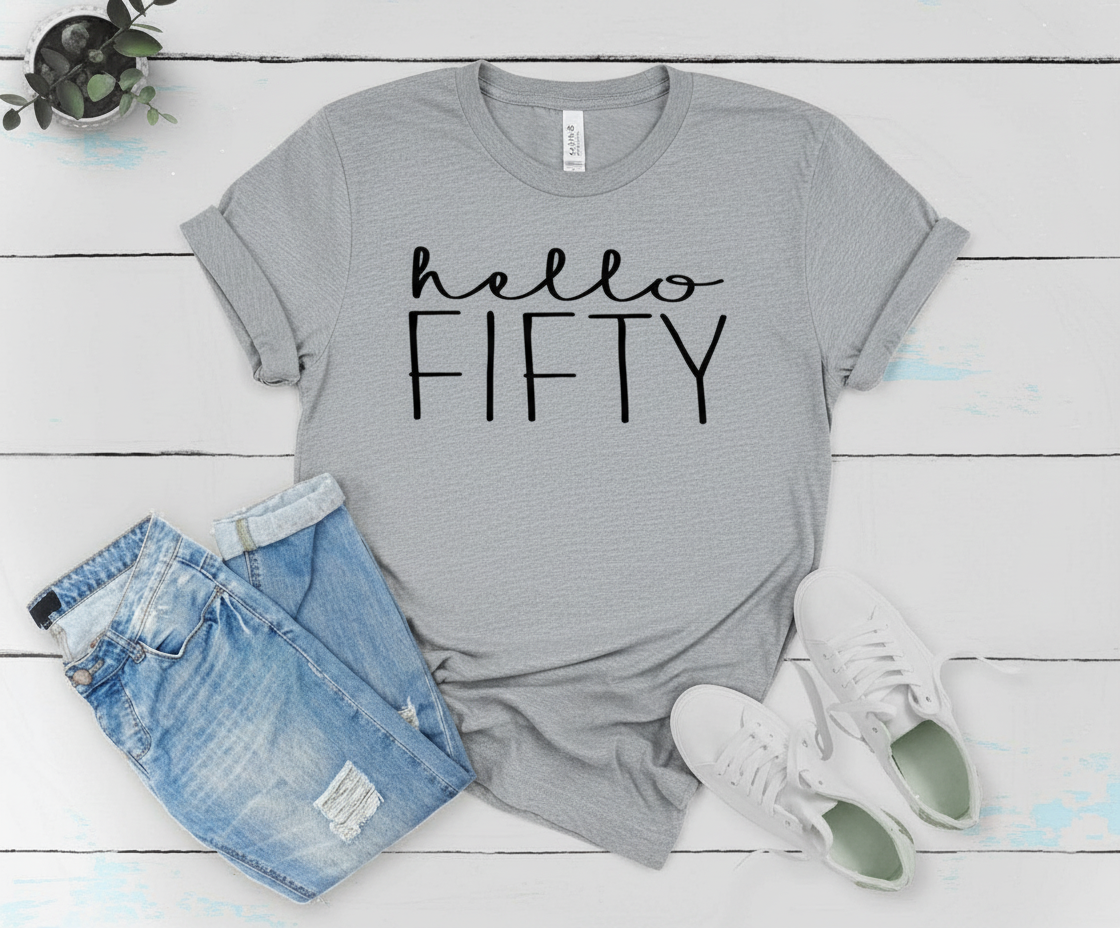 Gray t-shirt with 'hello FIFTY' text, paired with denim shorts and white sneakers on a light wooden floor.