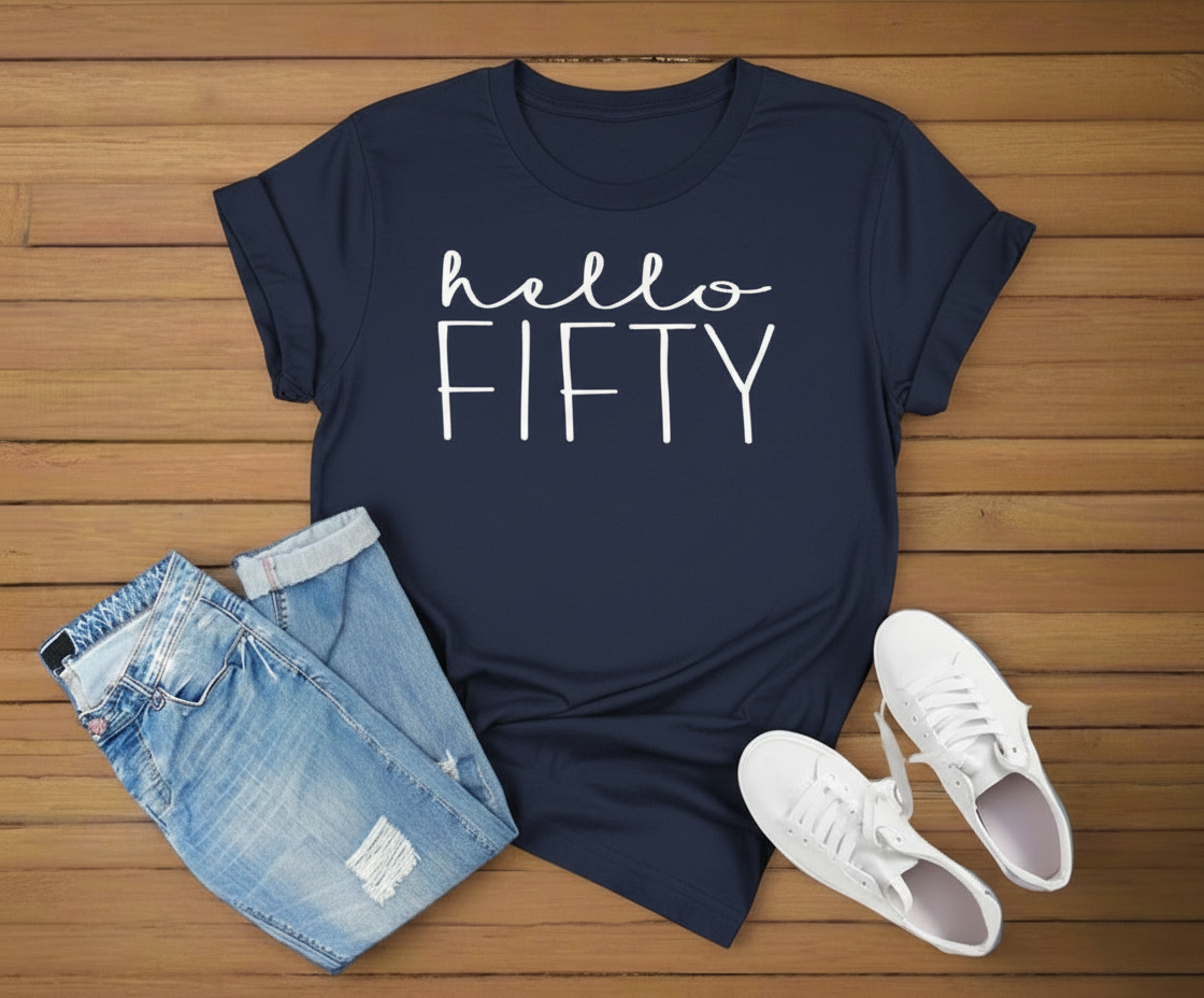 Navy blue t-shirt with 'hello FIFTY' text, denim shorts, and white sneakers on a wooden surface